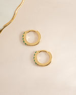 Gold 7mm emerald huggie earrings by Sami Jewels shown in a side view with vibrant green emeralds and sleek gold setting.