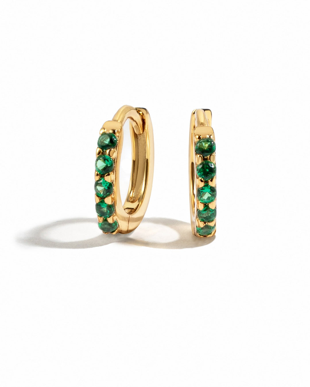 Gold 7mm emerald huggie earrings by Sami Jewels with vibrant green emerald stones on a white background.