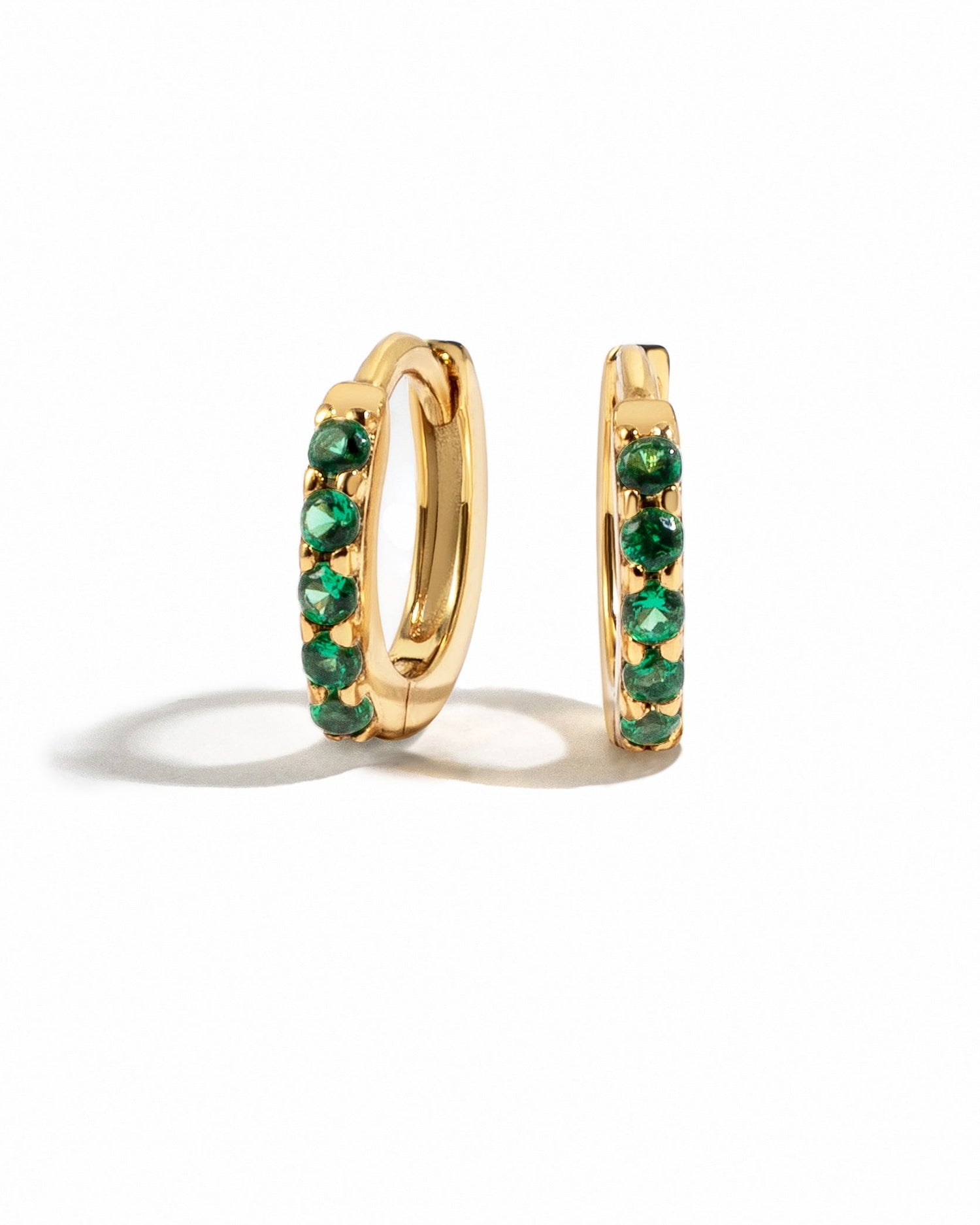 Gold 7mm emerald huggie earrings by Sami Jewels with vibrant green emerald stones on a white background.
