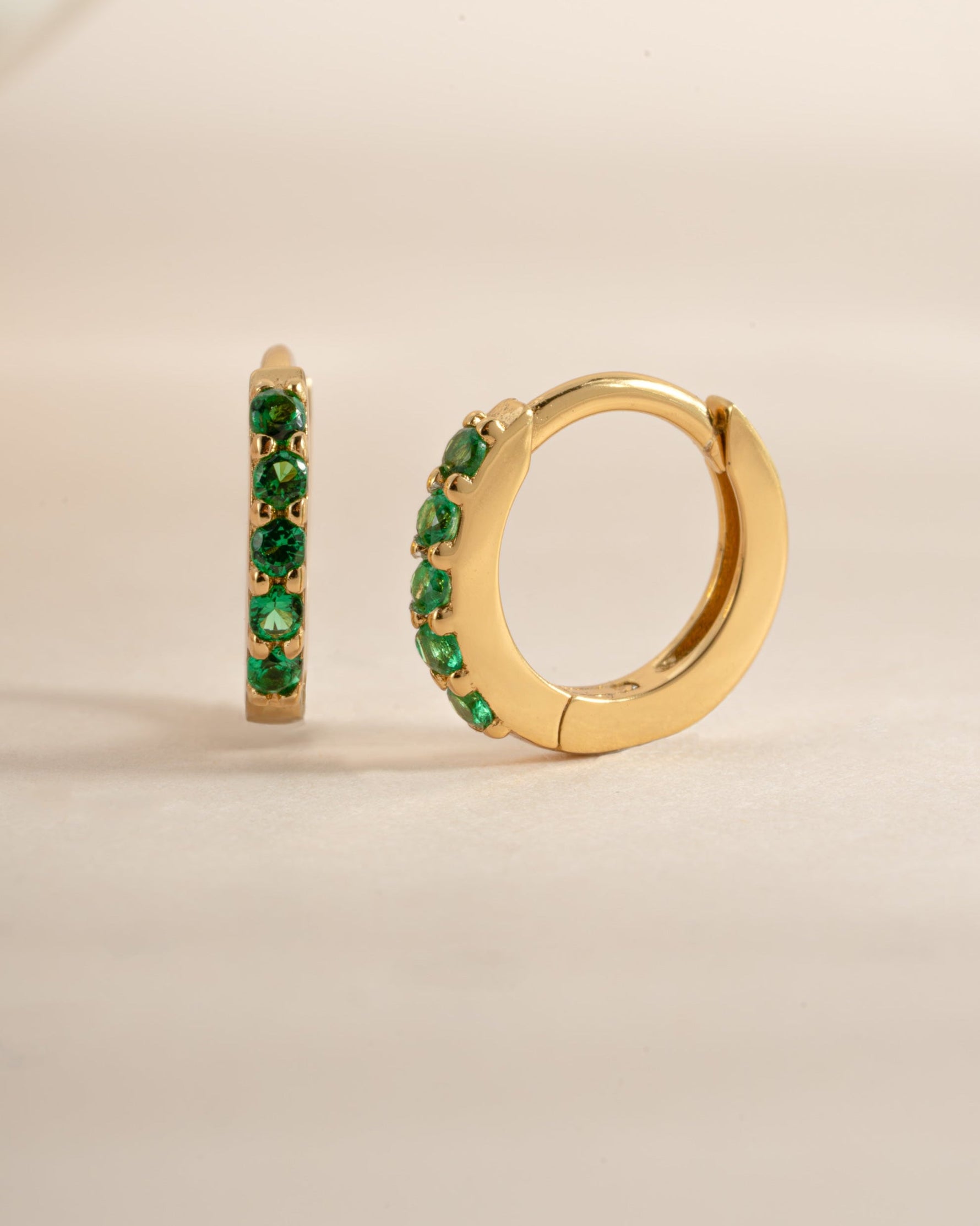 Gold 7mm emerald huggie earrings by Sami Jewels featuring vibrant green gemstones and a secure hoop design.