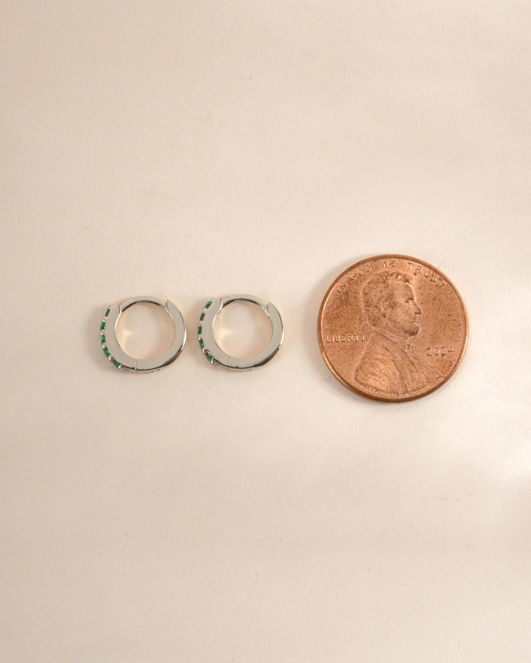 Sterling silver 7mm emerald huggie earrings with side profile view, showcasing the vibrant green gemstones and sleek design.