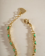 A gold bracelet with oval emerald gemstones alternating with white round stones and an adjustable clasp.