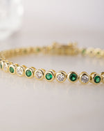 Gold bracelet with emerald green and white gemstones on a light background