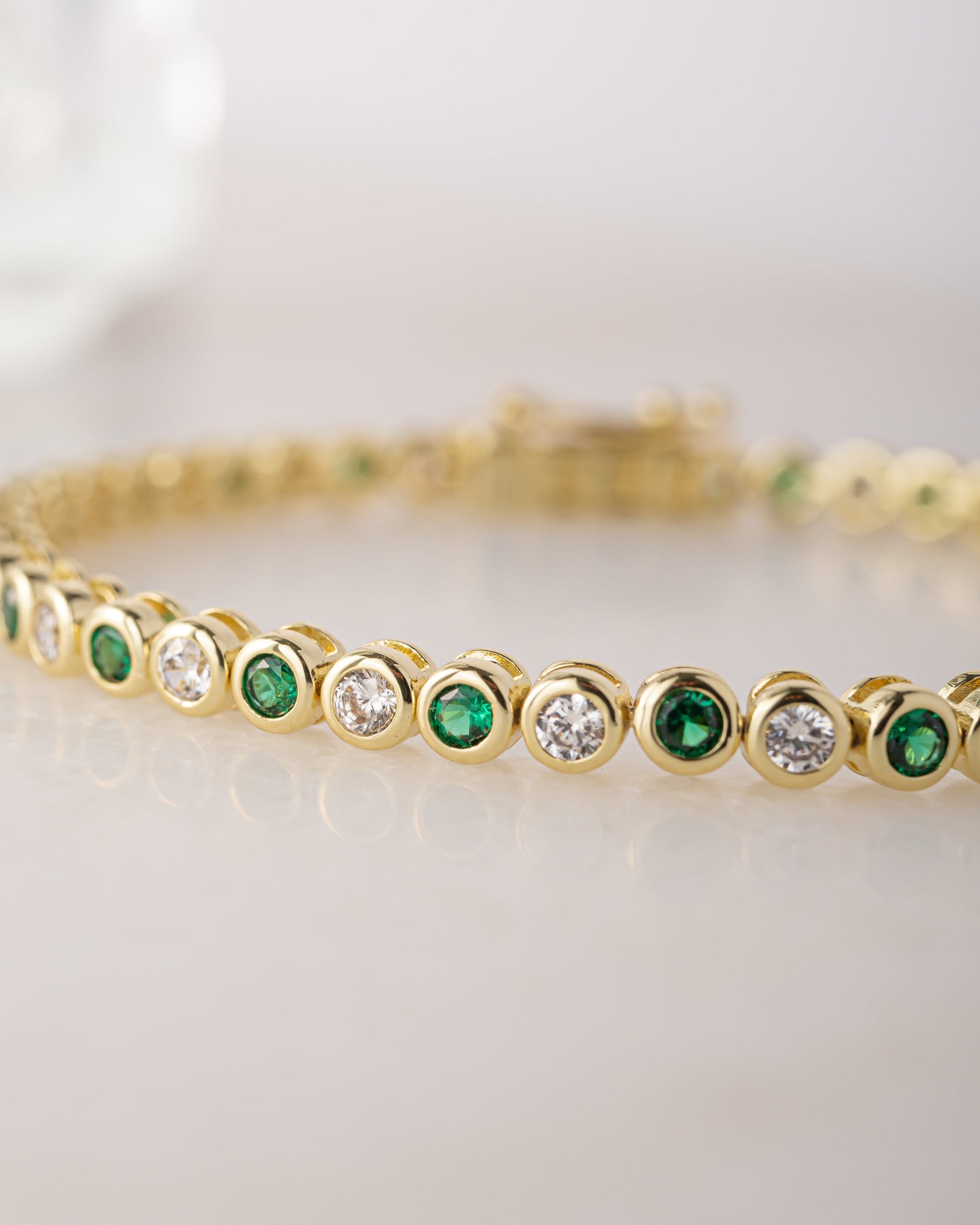 Gold bracelet with emerald green and white gemstones on a light background