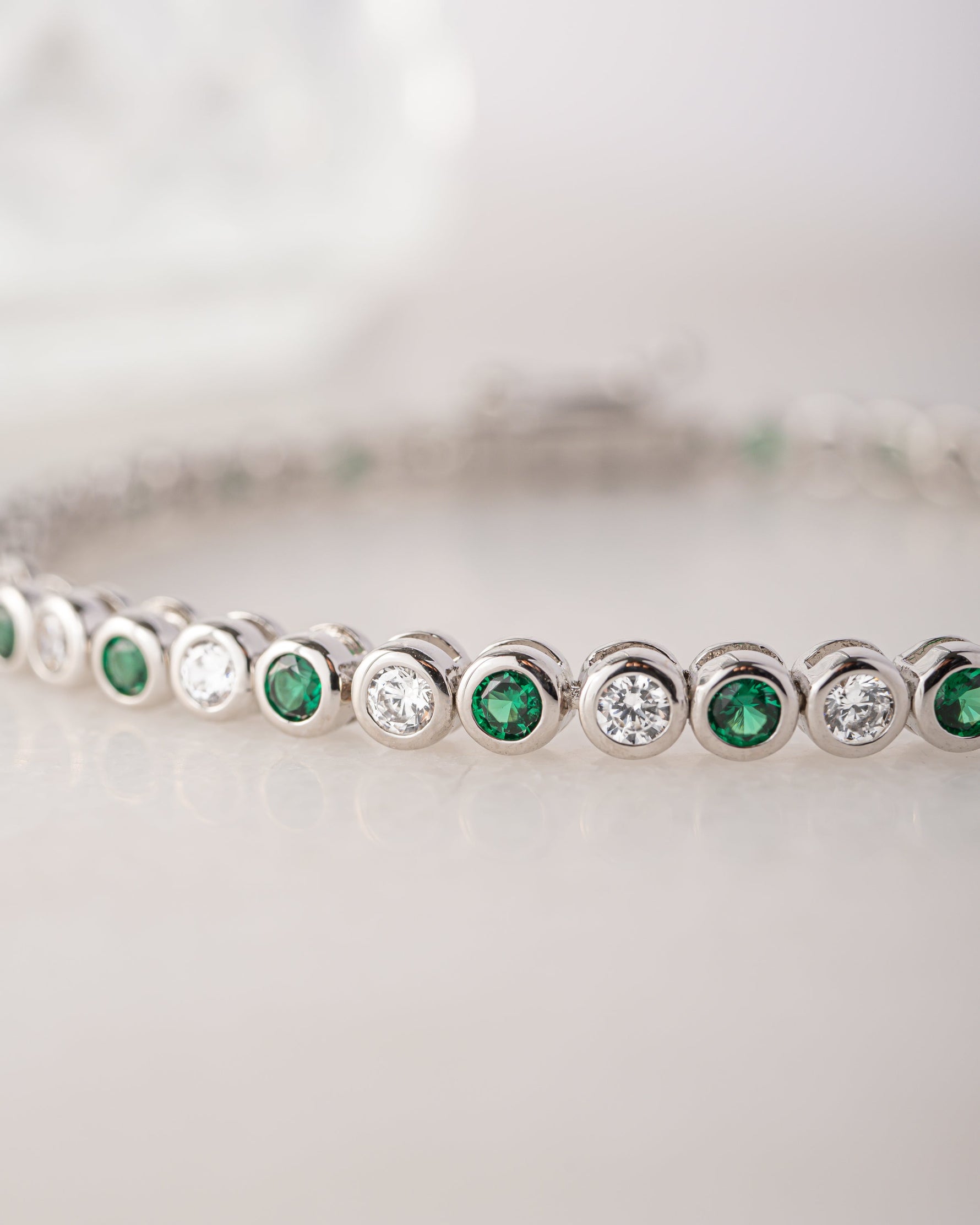 Silver bracelet with emerald green and white gemstones on a light background