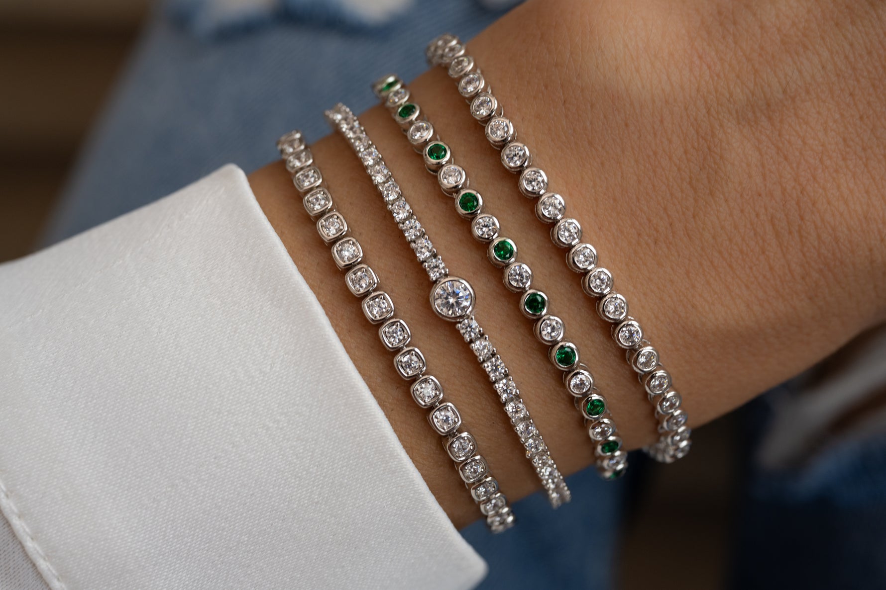 model wearing silver tennis bracelet stack featuring a round bezel tennis bracelet, a emerald green and white cz tennis bracelet, a round bezel charm tennis bracelet and a square bezel tennis bracelet