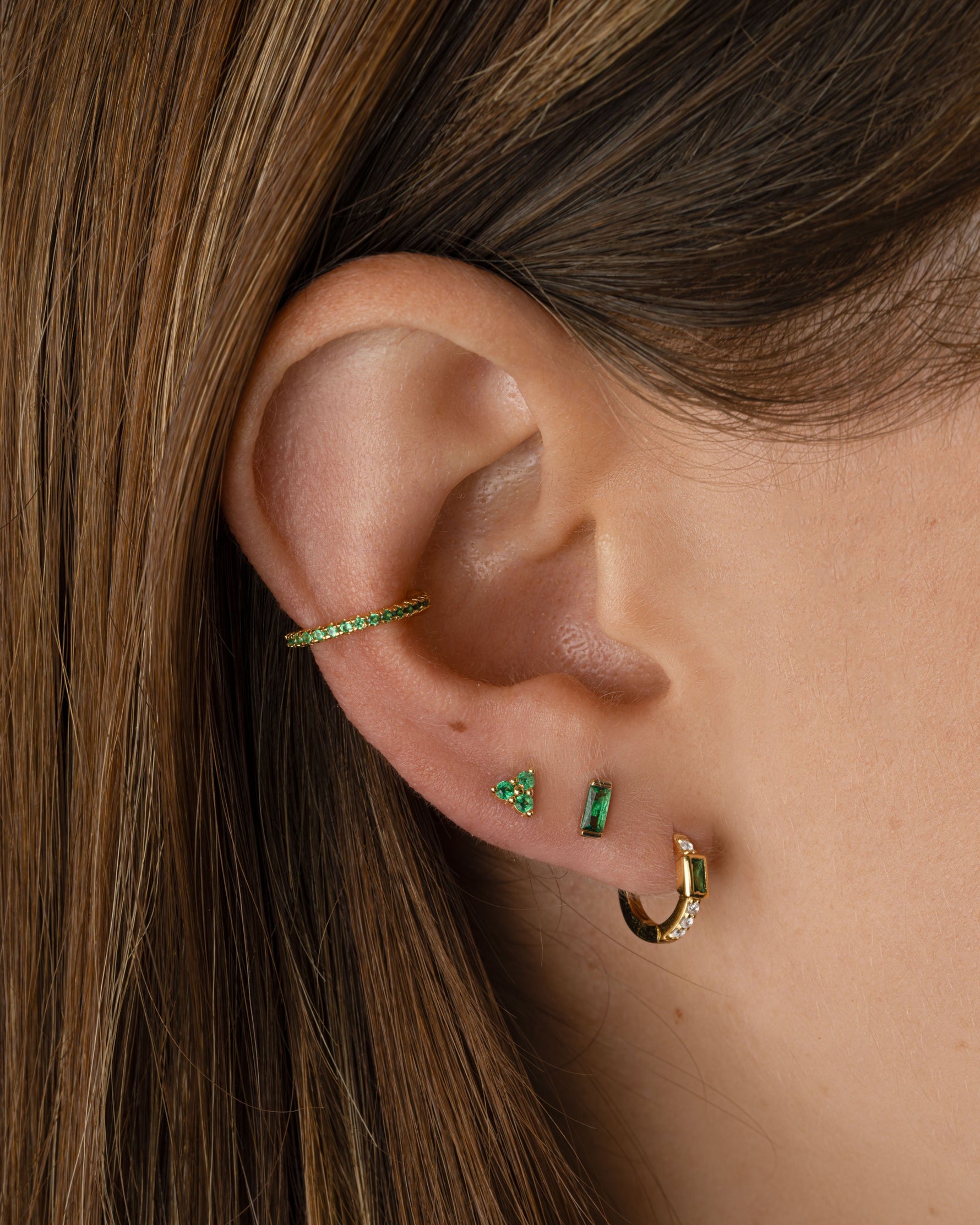 Sami Jewels tiny emerald 3-stone stud earrings with gold setting, featuring vibrant green emeralds on a model.
