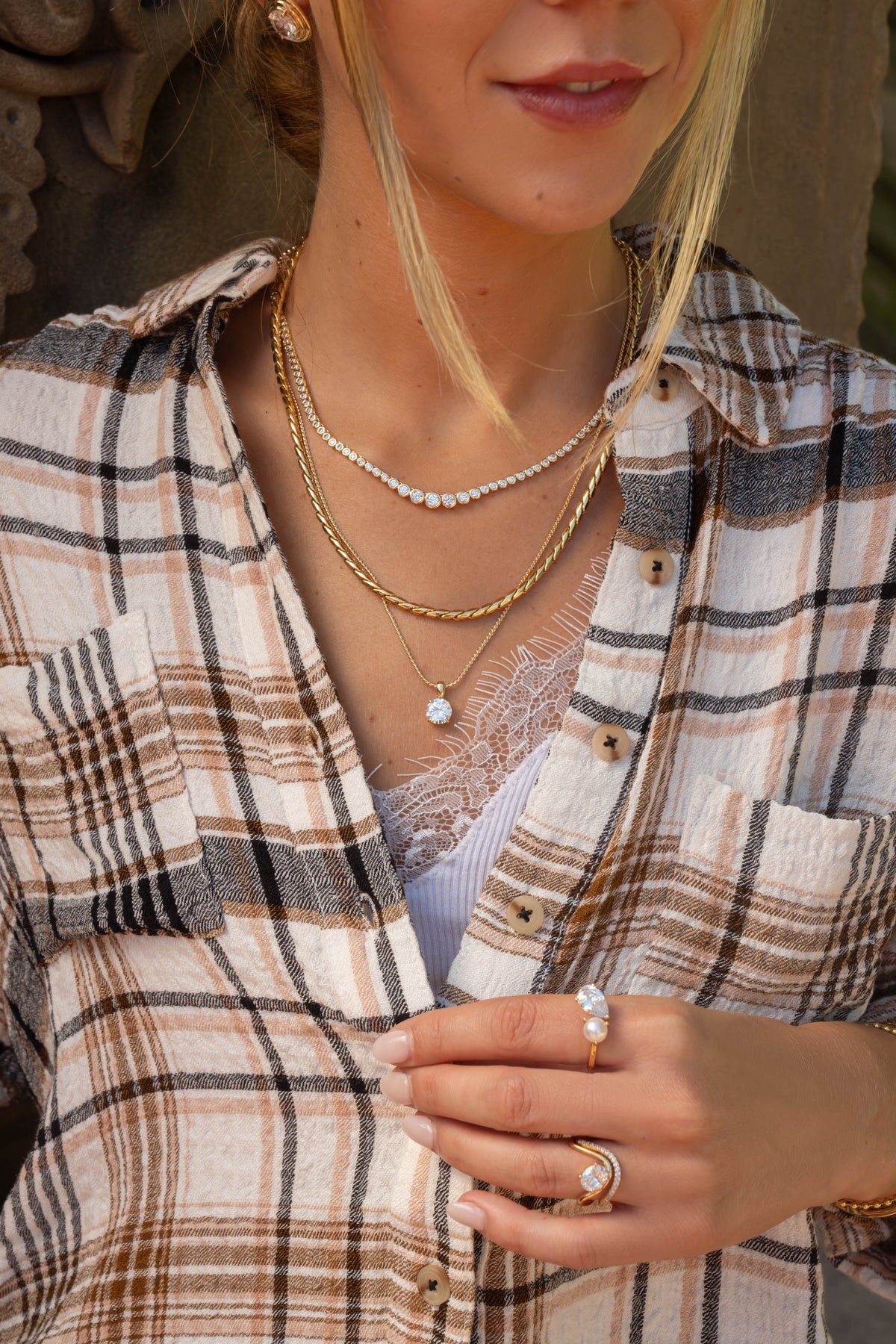 Gold graduated CZ tennis necklace, chunky chain and CZ solitaire pendant layered over a plaid shirt, with a pearl toi et moi ring and oval CZ ring set