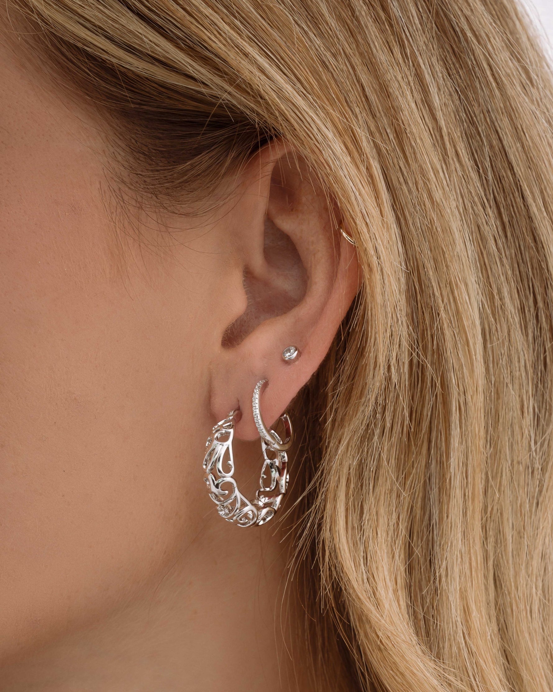 Silver filigree tapered hoop earrings stacked on a model showcasing intricate jewelry design.