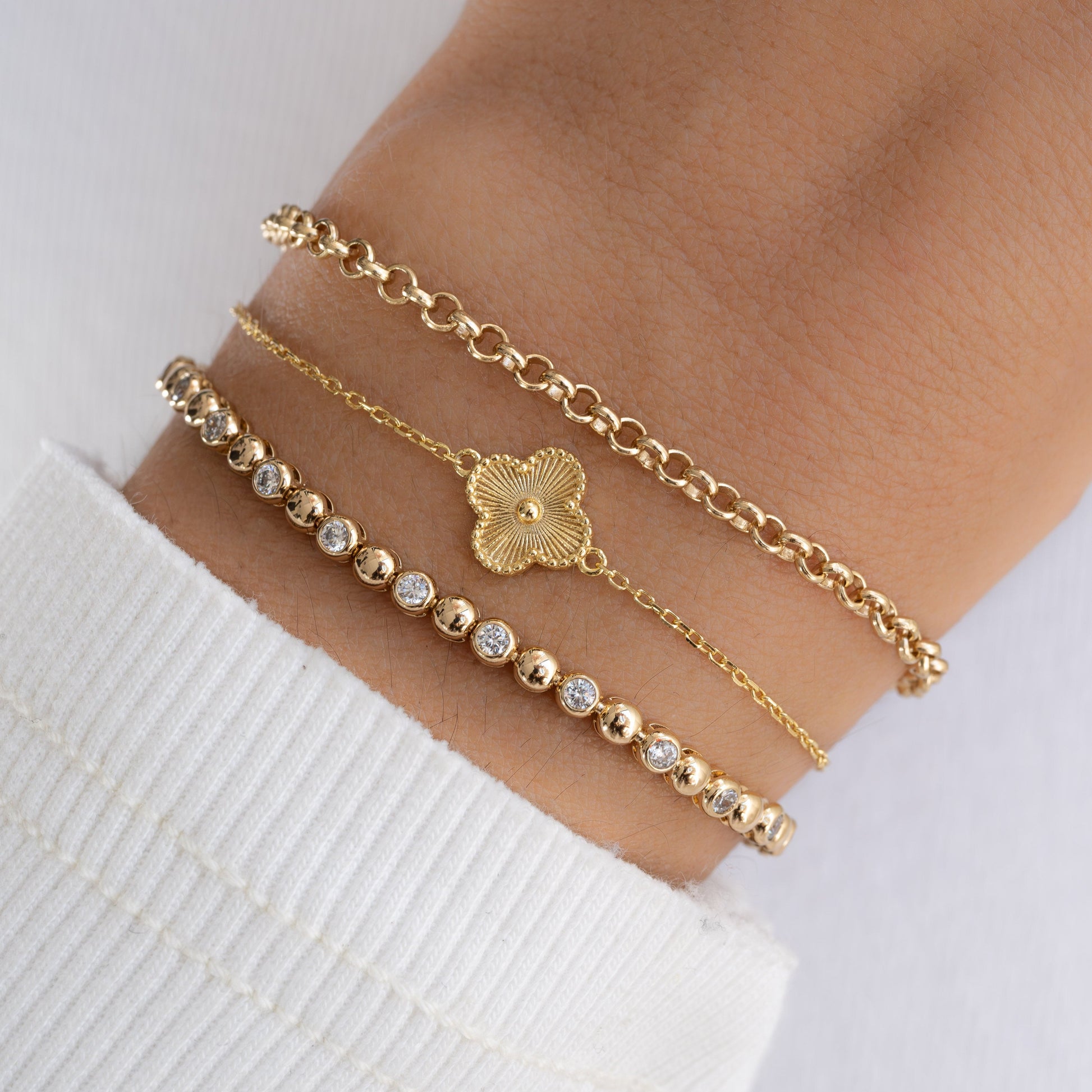 Model stacking a four leaf clover bracelet with a gold chain bracelet and diamond tennis bracelet.