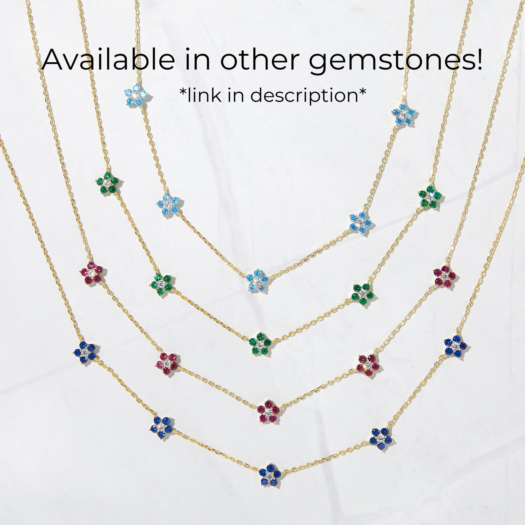 multiple colors gemstone flower necklaces from Sami Jewels on white background. Blue, emerald green, ruby red and sapphire blue flower diamond pendants on thin dainty chain.