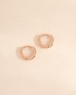 Rose gold Sami Jewels geometric pattern huggie earrings shown from a side view with intricate design.