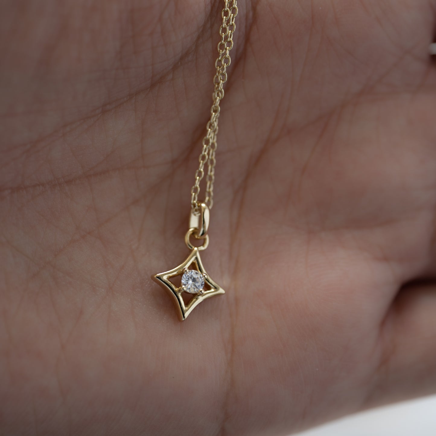 A hand showcasing a gold layering necklace with diamond shaped pendant
