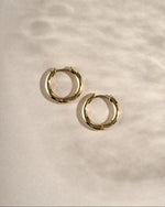gold 12mm gold hoop earrings with latch back closure on a simple beige background