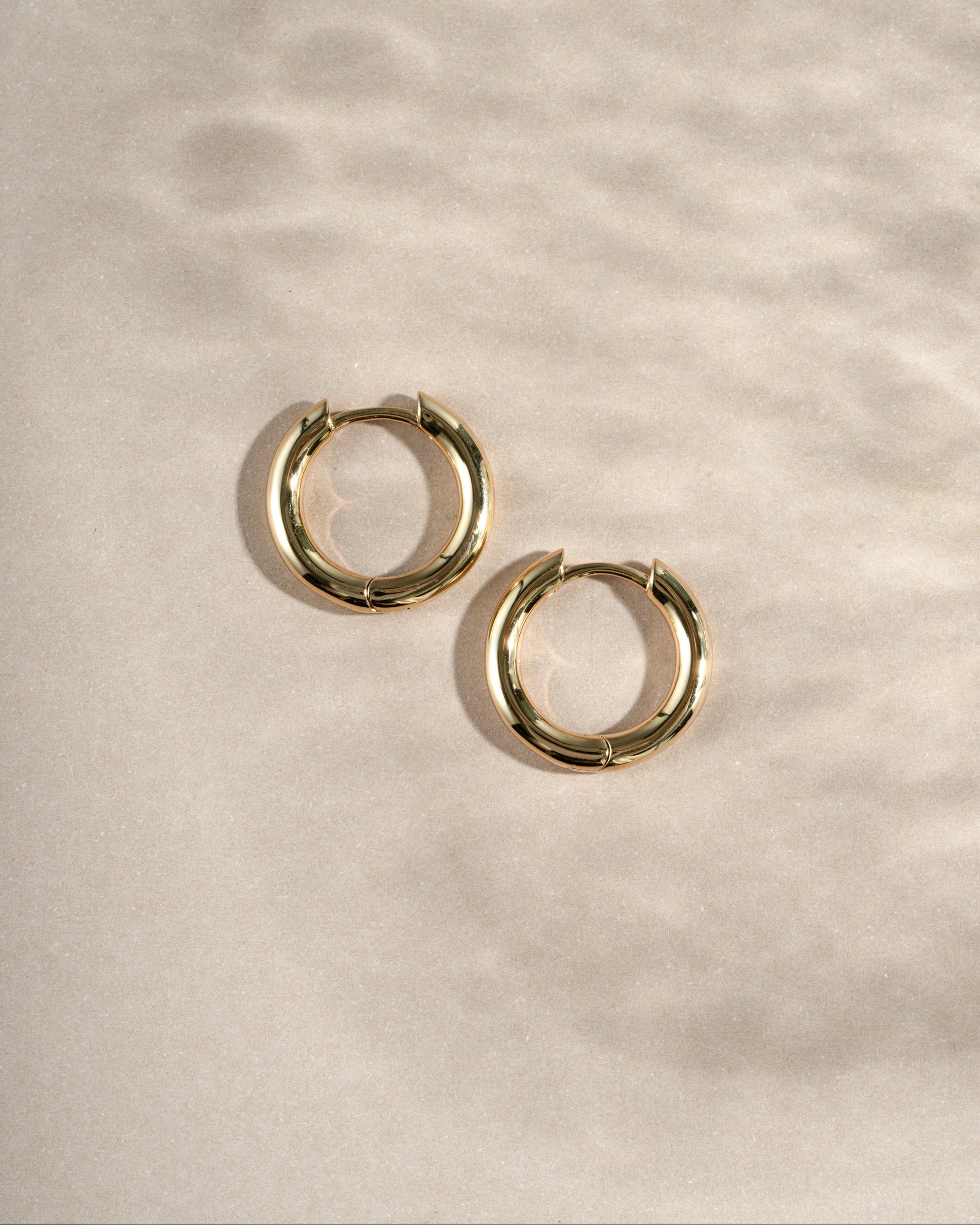 gold 12mm gold hoop earrings with latch back closure on a simple beige background