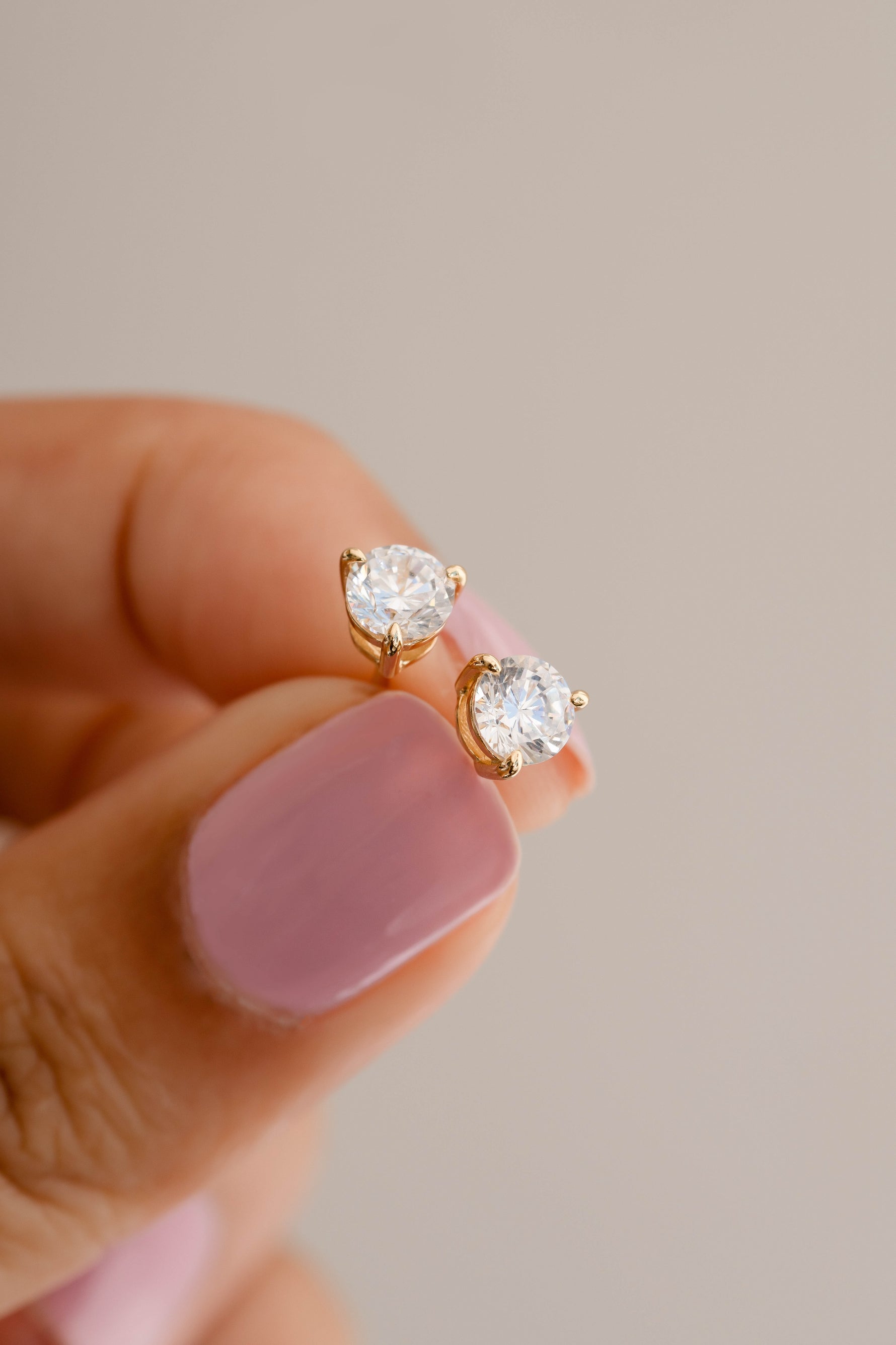 gold round solitaire diamond stud earrings helld between fingers 
