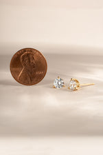 gold 5mm round solitaire diamond earrings being compared to size of penny 