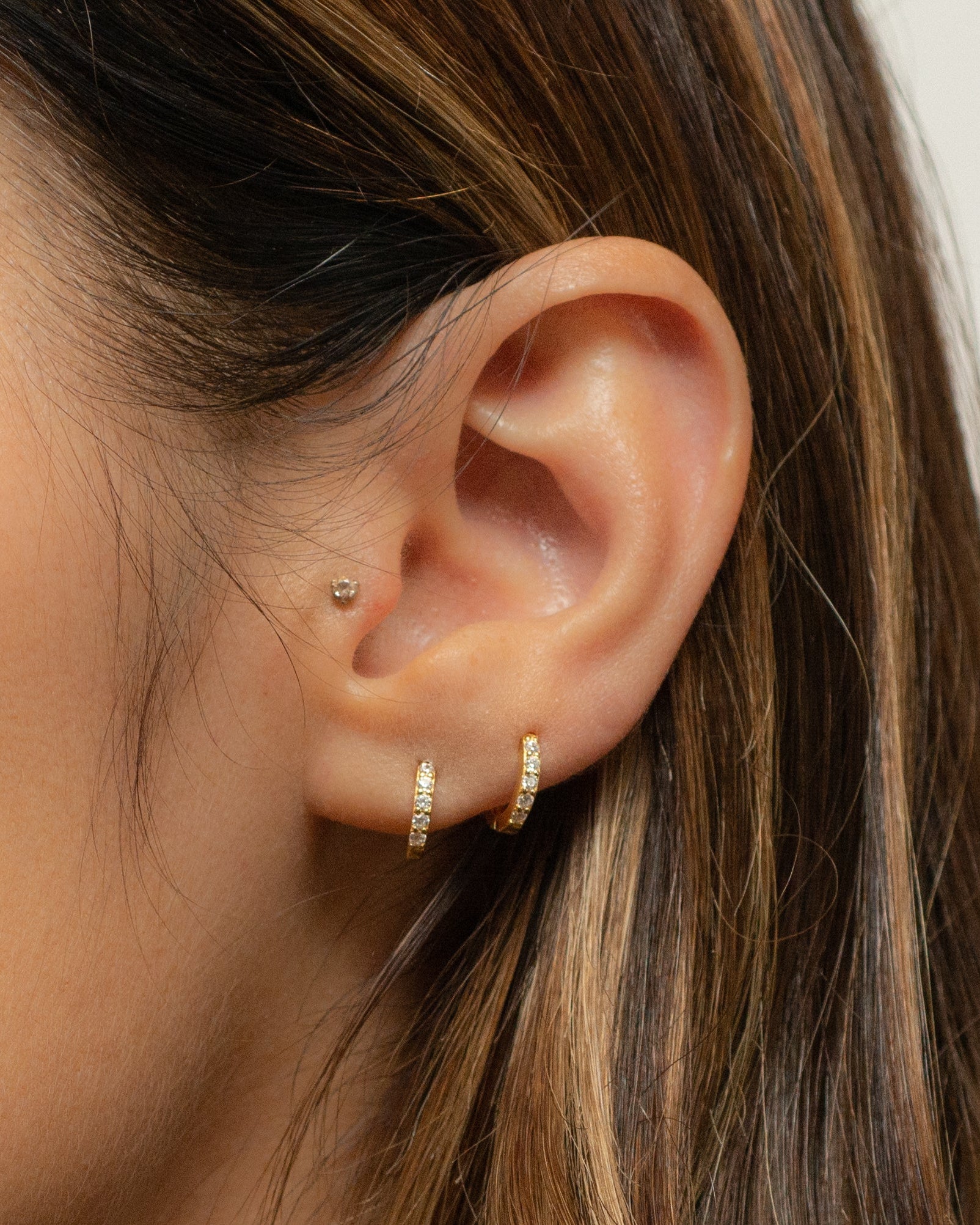 Women wearing gold 7mm diamond huggie earring in her first and second hole ear piercing