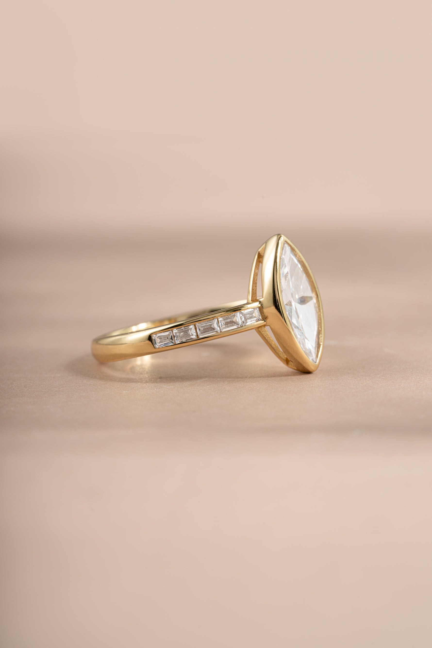 Gold bezel marquise ring with baguette band by Sami Jewels, showcasing a sleek design with marquise gemstone and baguette accents.
