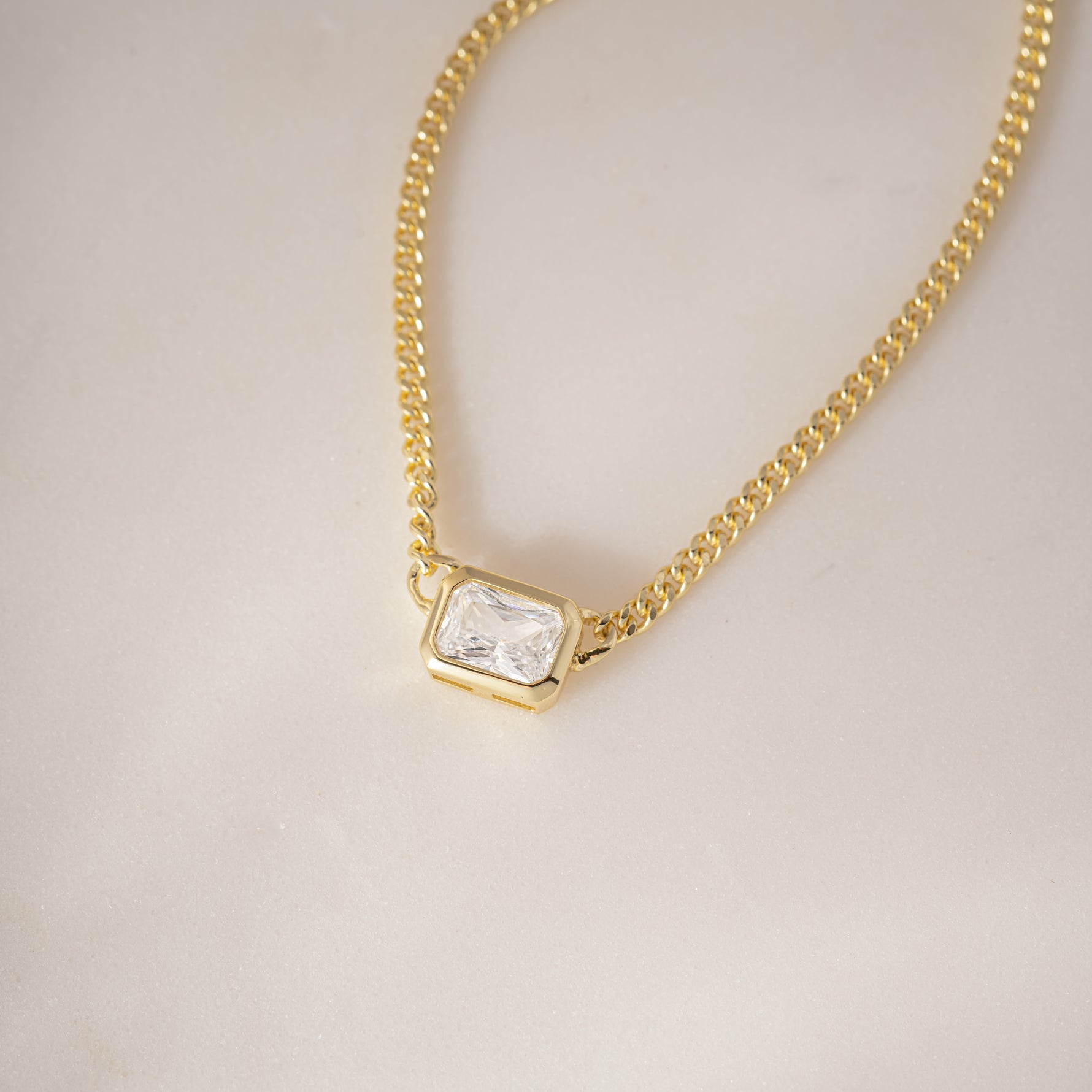 Detailed shot of Bezel Set Emerald Cut Necklace, highlighting the smooth, tactile edges of the gold setting.