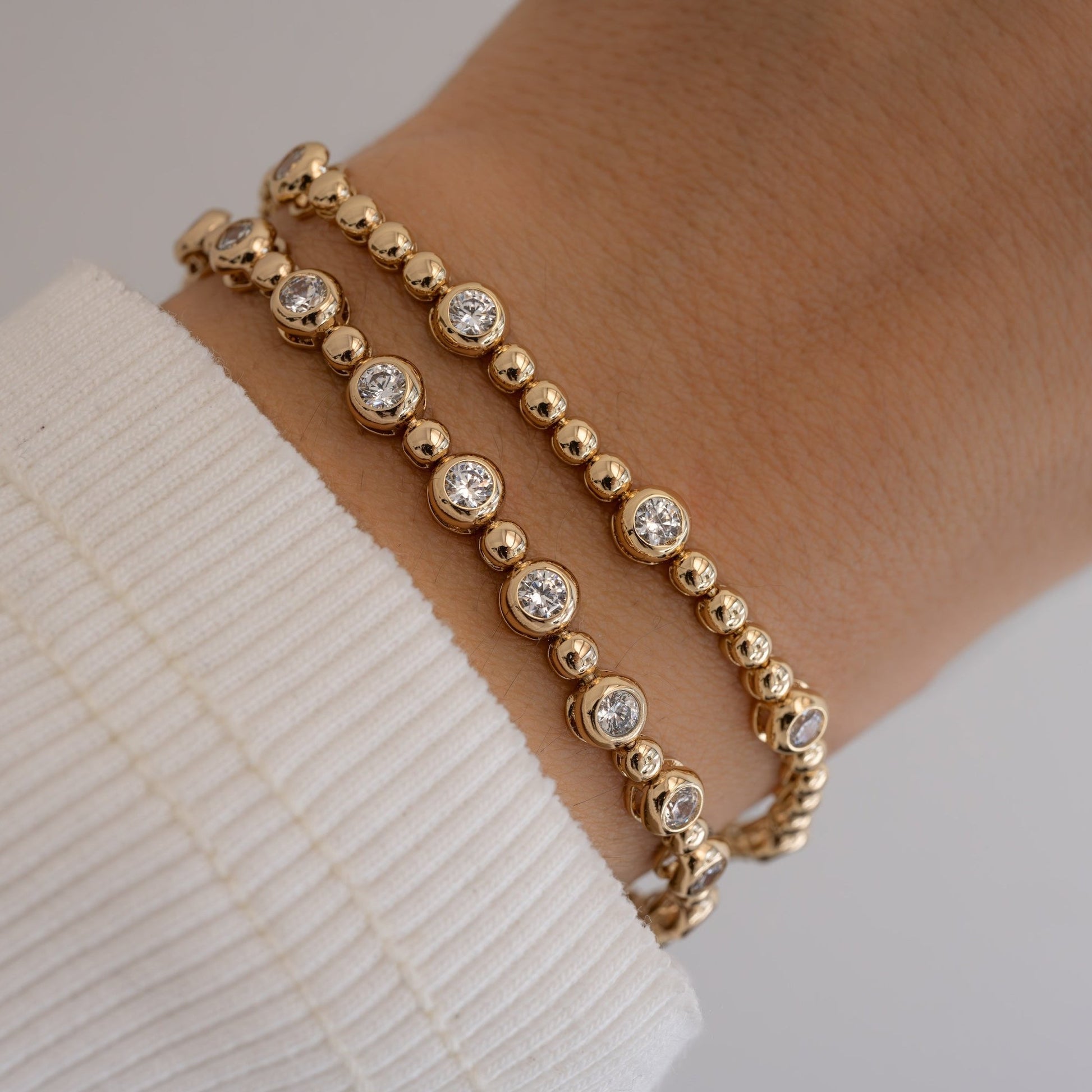 Gold tennis bracelet with small and large bezels stacked with beaded bracelet.