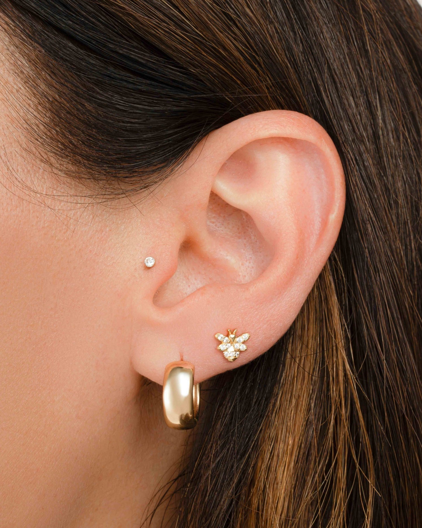 model wearing gold jewelry featuring a gold hoop earring and a tiny bee stud earring 