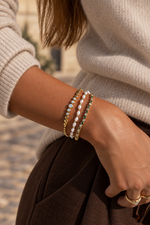 Gold graduated bezel tennis bracelet styled in a three-bracelet stack with a beige sweater.