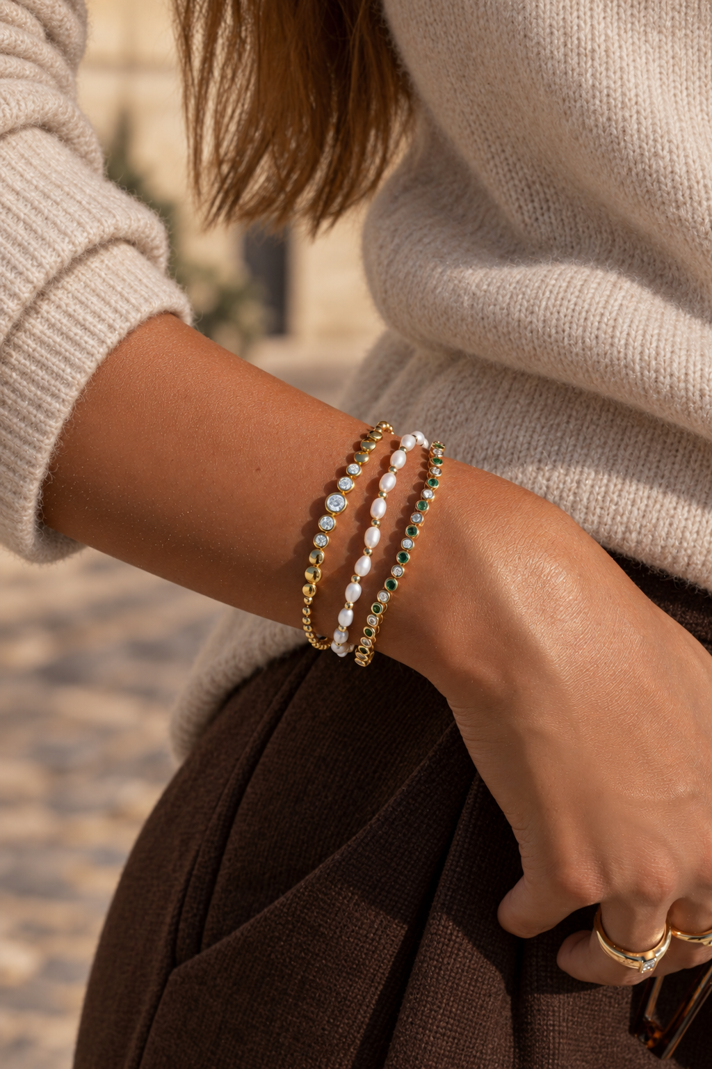Gold graduated bezel tennis bracelet styled in a three-bracelet stack with a beige sweater.