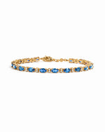 A gold tennis bracelet featuring a row of oval-cut blue gemstones with alternating white round stones.