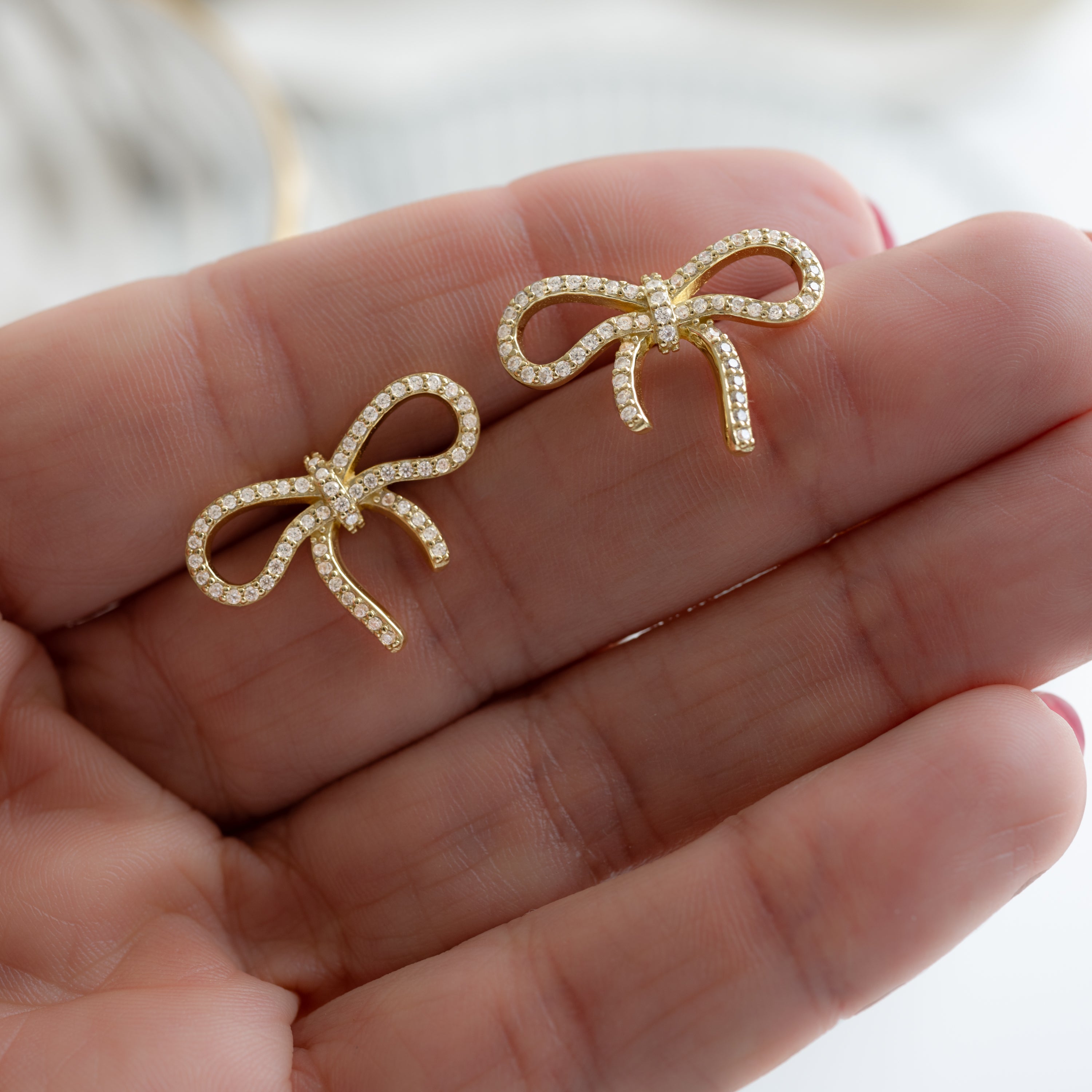 dainty earrings with a tiny bow accent, held on a palm.