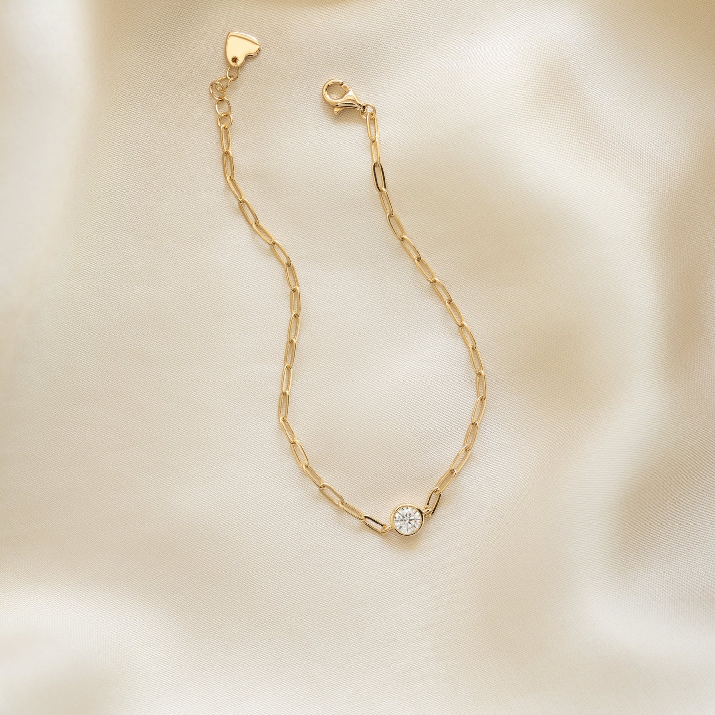 Dainty gold diamond chain bracelet with round diamond charm on silk background