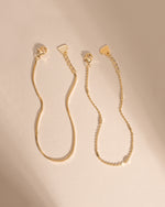 Two gold bracelets laid side by side, showing their lobster clasps, extenders and heart-shaped tags.