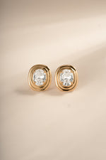 Front view of gold oval bezel statement studs on a cream background.