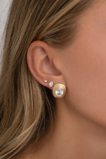 Close-up of a gold oval bezel statement stud on an ear, with smaller oval and round studs.