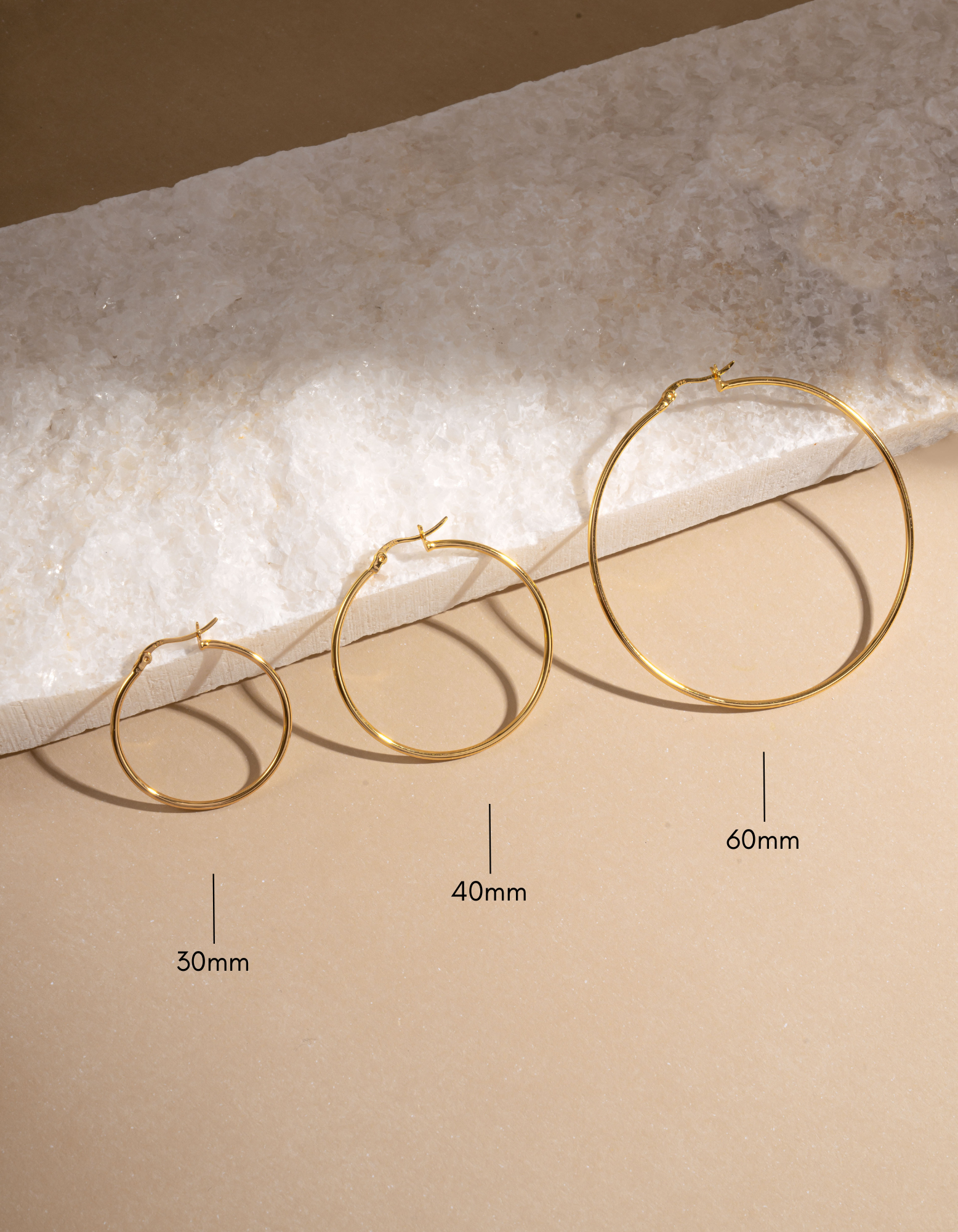gold classic hoop earrings with different sizes, one 30mm gold hoop earring, one 40mm gold hoop earring, and one 60mm gold hoop earring on a neutral background