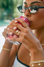 Model wearing a cute gold statement ring stack featuring a chevron wavy ring set with cz stones, an oval bezel ring, and a cz & plain double band ring, while drinking soda.