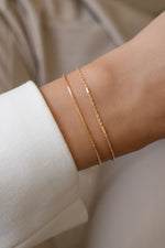 Gold box chain and satellite bracelets worn together on a model's wrist.