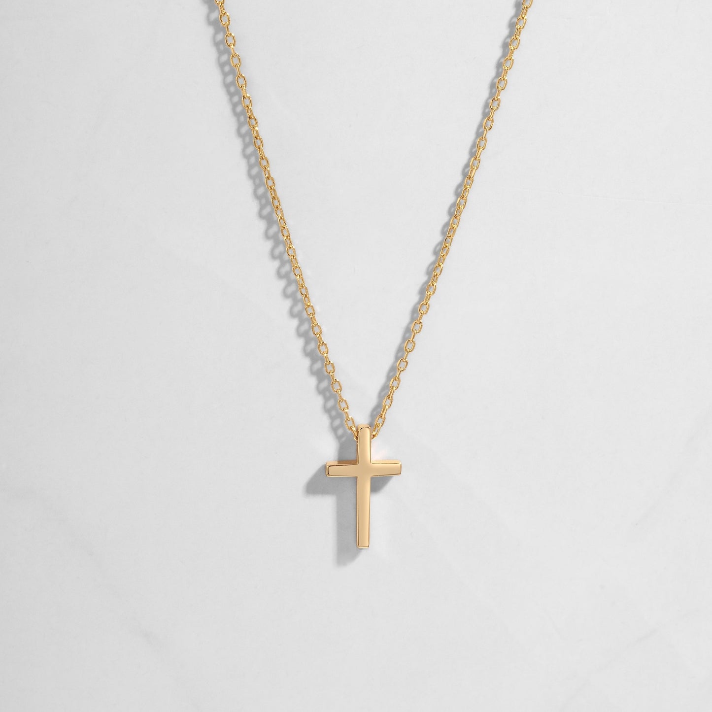 Dainty gold plain cross necklace on delicate chain on white background