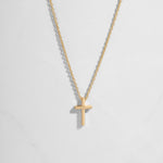 Dainty gold plain cross necklace on delicate chain on white background