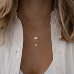 gold necklace stack featuring a freshwater pearl necklace, a halo emerald cut cuban link necklace, and a simple chain.
