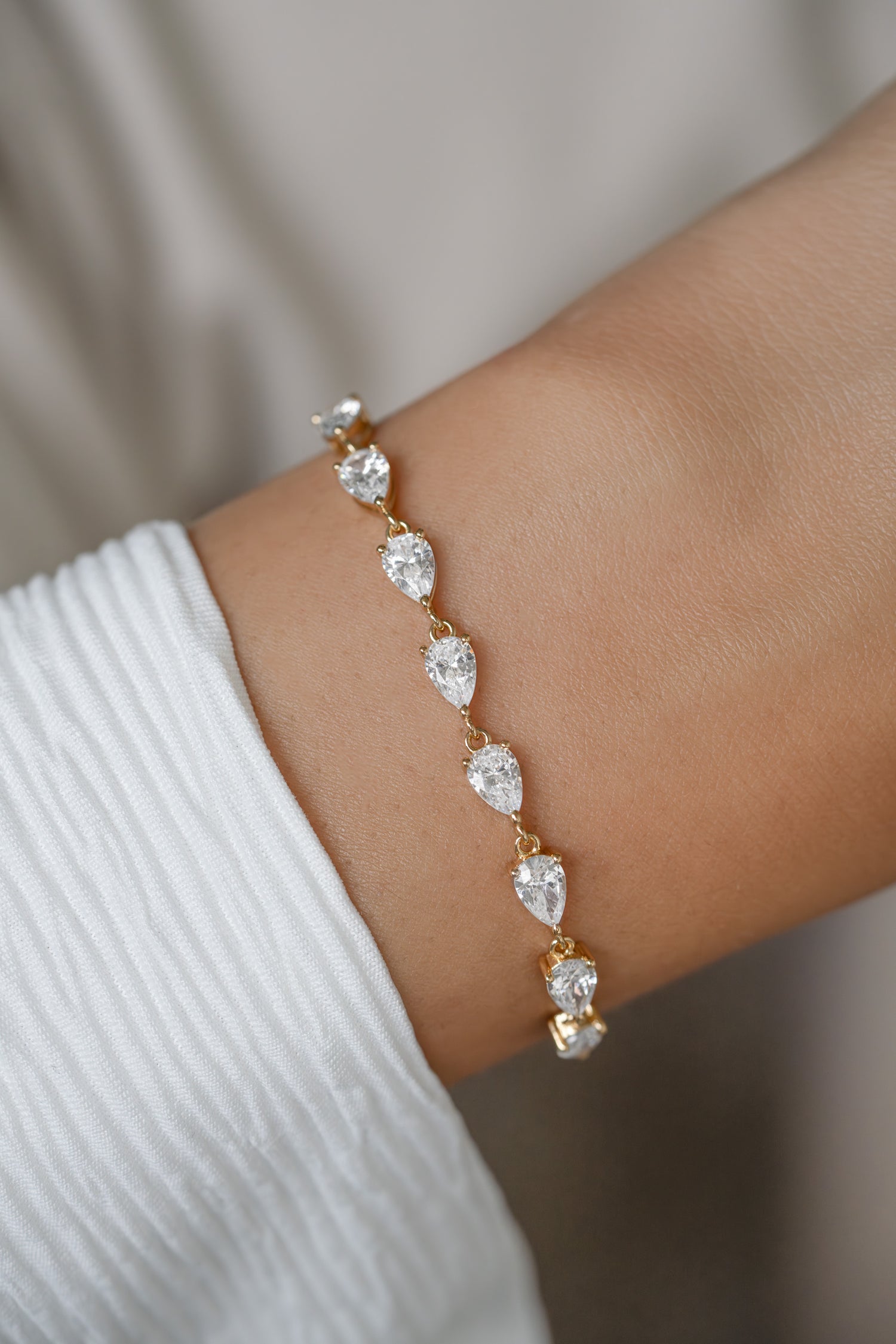 A gold bracelet with five pear-cut diamond stones worn on a person's wrist, paired with a white ribbed sleeve.