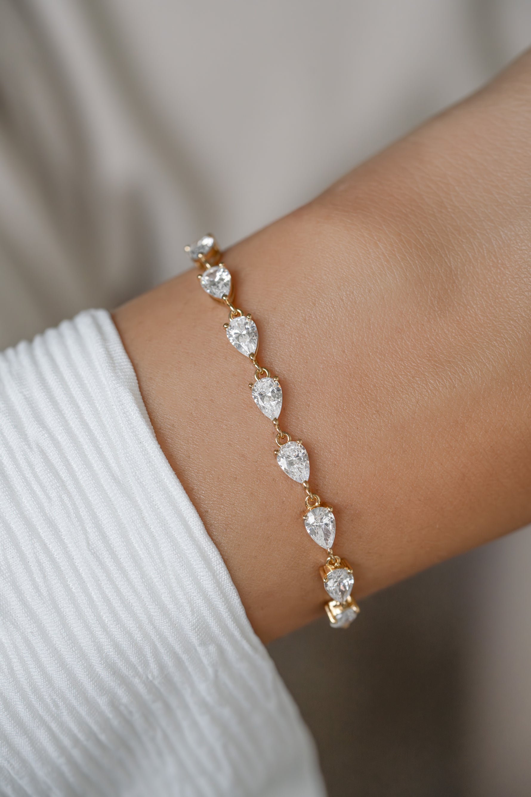 A gold bracelet with five pear-cut diamond stones worn on a person's wrist, paired with a white ribbed sleeve.