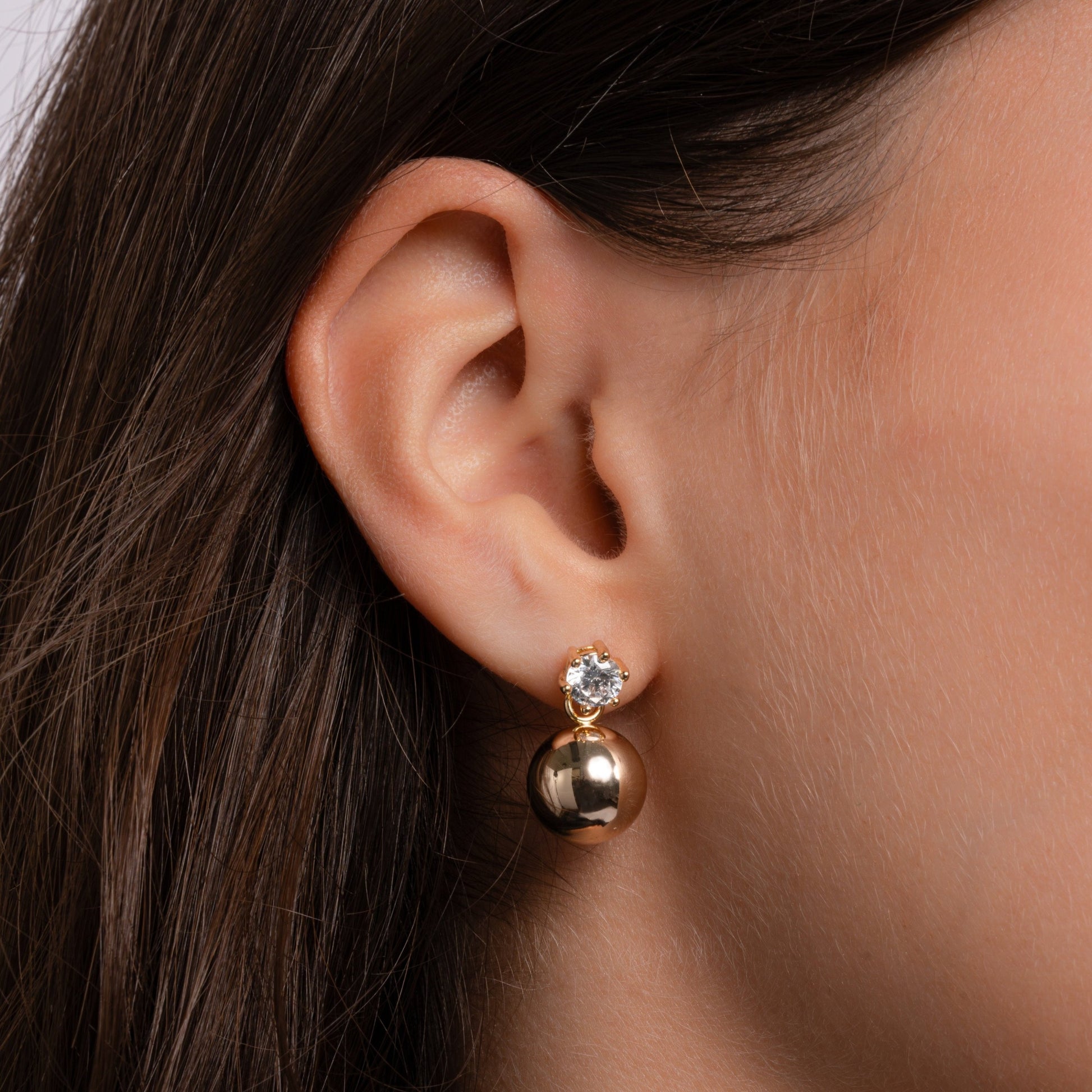 Model wearing tiny gold stud earrings with a dainty ball and diamond accent.