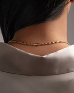 A close-up back view of a person wearing a delicate gold tennis necklace with a box clasp.