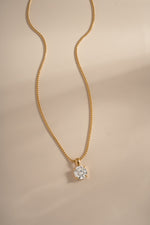 Gold round solitaire pendant and chain arranged on a cream background.