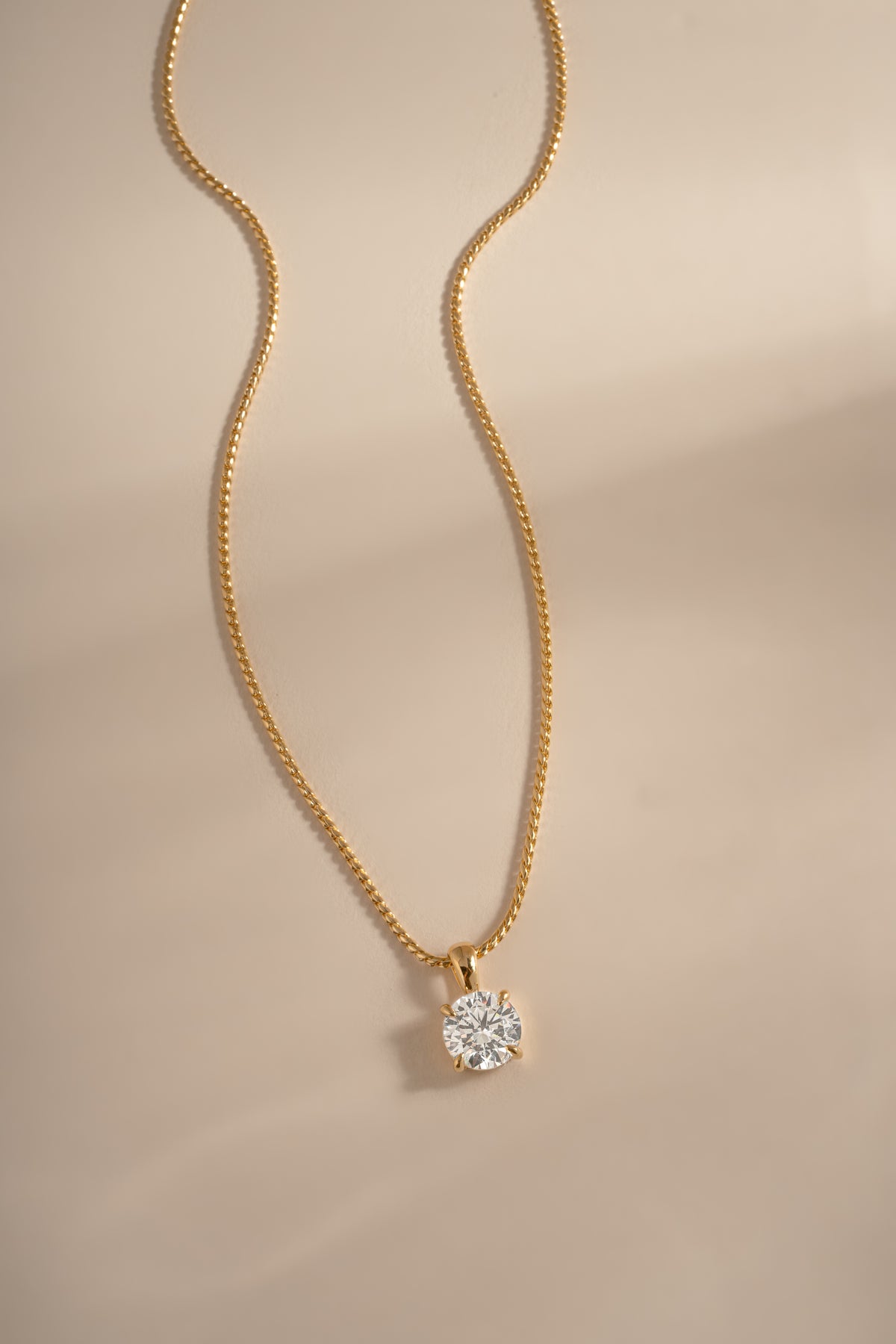 Gold round solitaire pendant and chain arranged on a cream background.