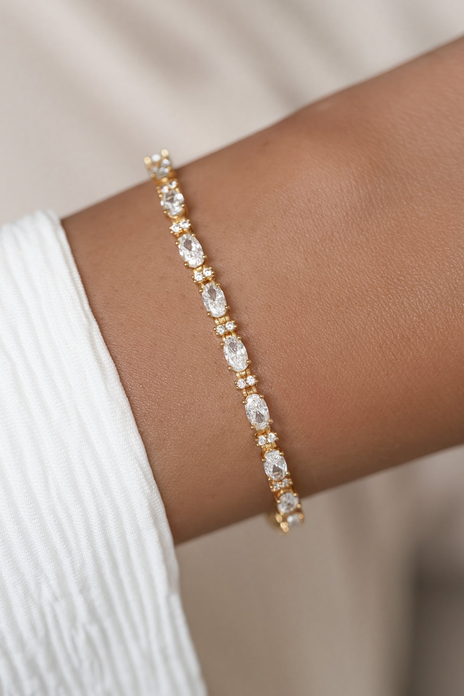 A gold tennis bracelet with clear oval-cut cubic zirconia stones modeled on a wrist. 