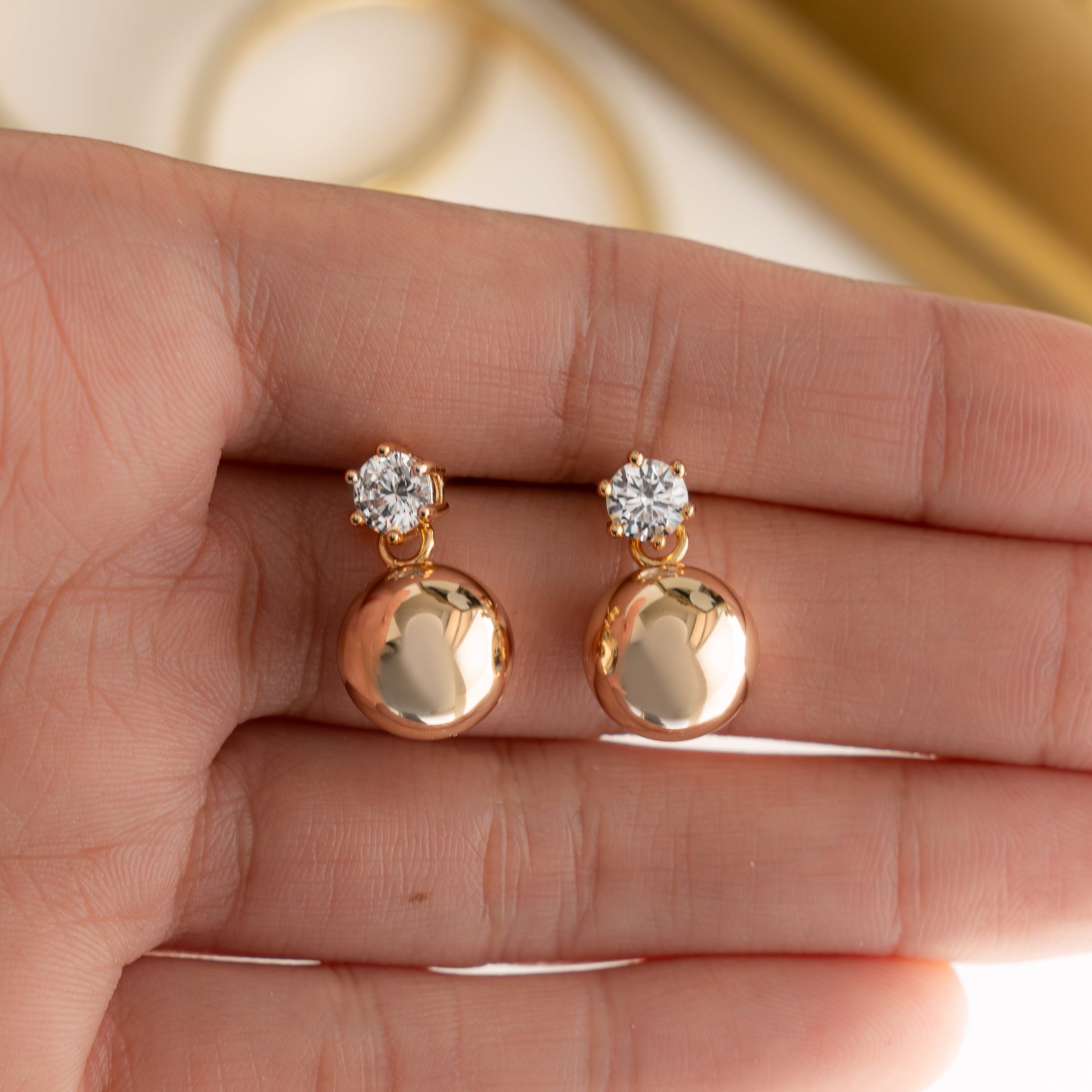 Closer view of intricate details of the tiny stud earrings in gold, held in hand