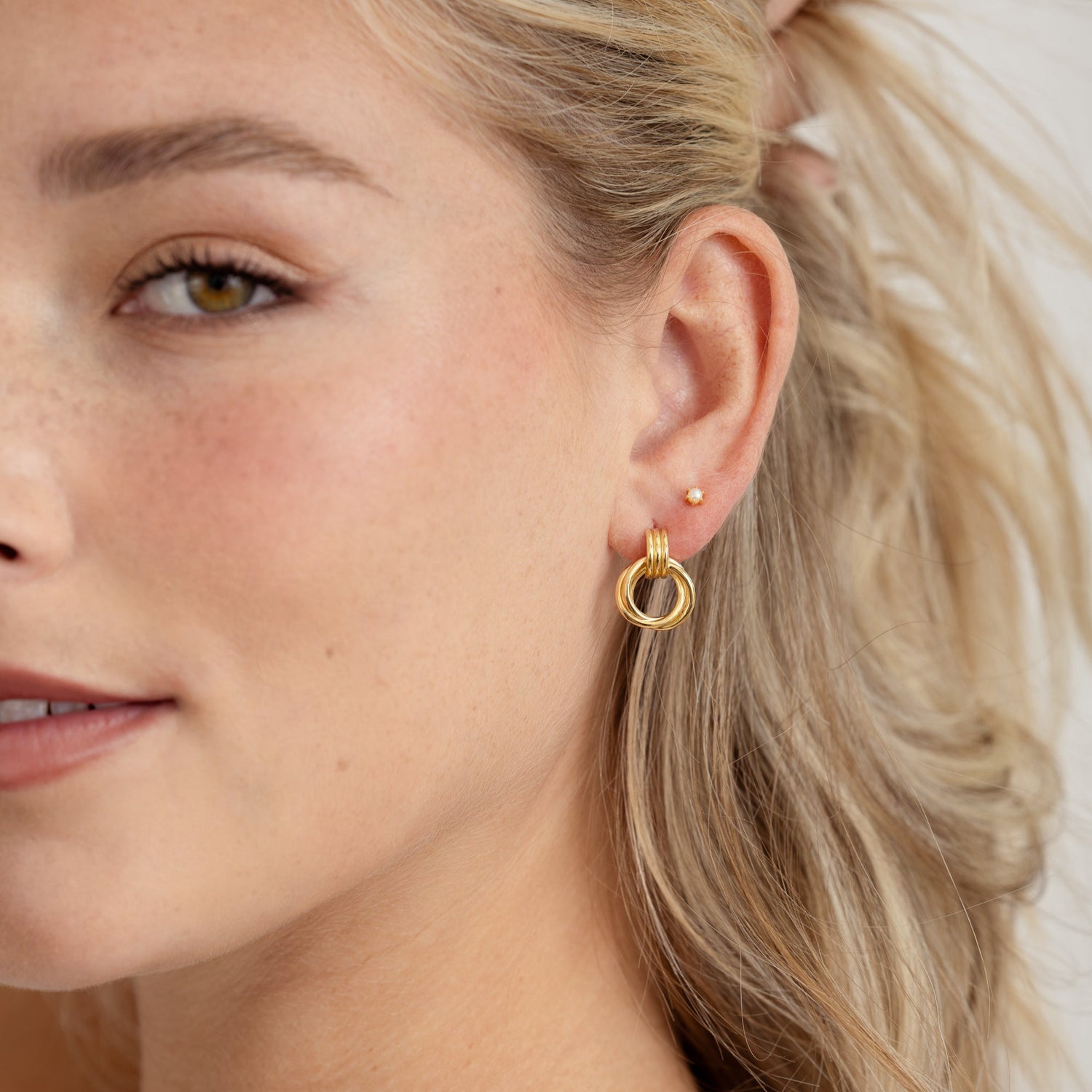 model wearing Knot Hoop Earrings stacked with dainty studs for a trendy layered ear look.
