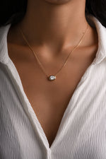 Gold east-west oval bezel pendant worn alone on a model in a white shirt.